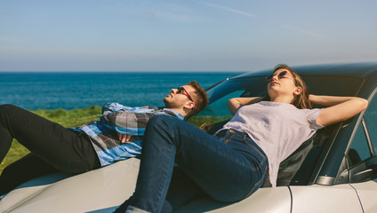 Young couple resting lying on the windshield and the hood of the car