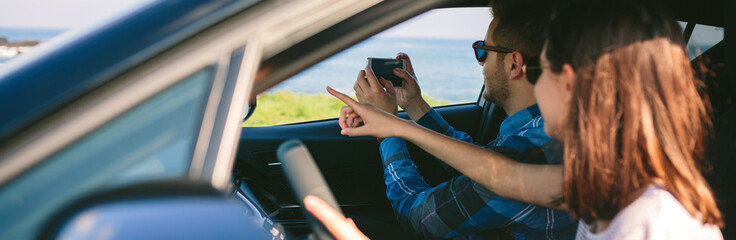 Couple traveling taking a picture of the landscape with the mobile from the car