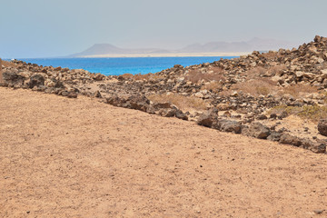 Spectacular landscape overlooking the blue sea from sand and rocks road with mountain in the background at Isla de Lobos, Fuerteventura, Canary Islands, Spain