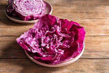 Plate with leaves of fresh red cabbage on wooden table