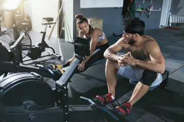 Fototapeta na wymiar Gym. Man And Woman Training On Rowing Machine At Crossfit Club 