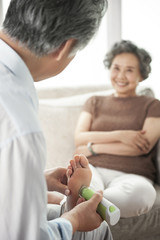 Obraz premium Old father helps mother to use pedicure to repair the dead skin on his feet, very happy