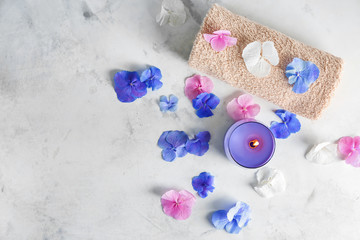 Burning candle with towel and hydrangea flowers on light table