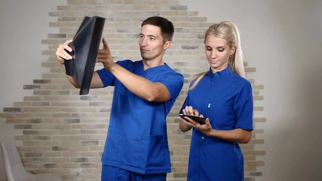 Team of cooperating doctors work together examining x-ray picture. Doctors or interns in blue uniforms work with tablet. 4k
