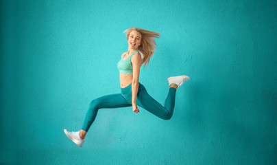 Sporty woman jumping near color wall - obrazy, fototapety, plakaty