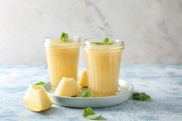 Glass jars with delicious melon smoothie on light table