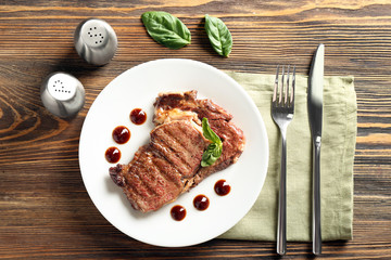 Plate with delicious grilled steak and sauce on wooden table