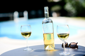 two glass of cool white wine with bottle outdoor in a restaurant pool side terrace in sunny summer day