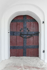 Antique wooden door with wrought iron handles and chain on whitewashed wall background.