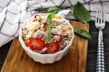 Bowl with tasty boiled rice and vegetables on board