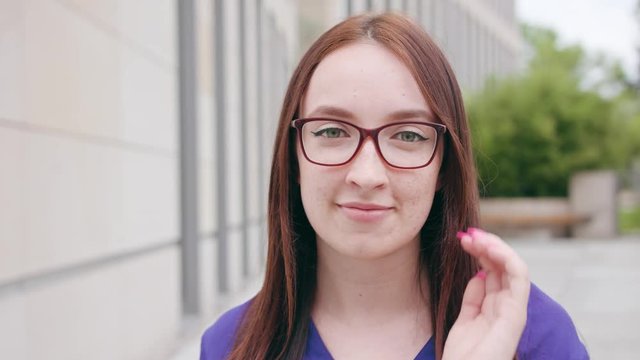 A happy smiling brunette woman wearing glasses in the city street. Close-up shot. Soft focus