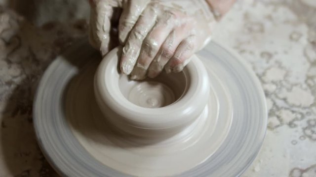 Close up with top view of hands of male potter throwing bowl out of wet clay on spinning pottery wheel