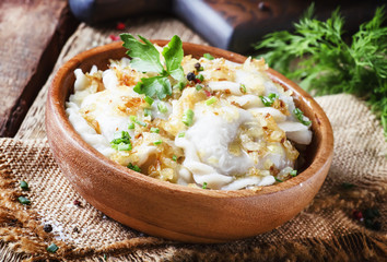 Traditional Russian vareniki with potatoes and fried onions in bowl on old wooden table, rustic style, selective focus