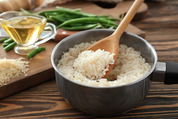 Saucepan with boiled rice on wooden table