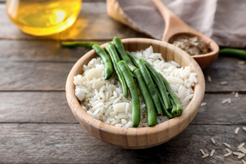 Bowl with tasty boiled rice and green beans on wooden table