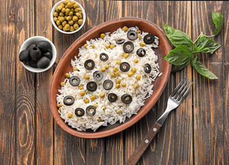 Plate with tasty boiled rice, olives and peas on wooden table