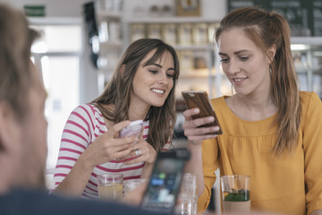 Two girlfriends meeting in a coffee shop, using smartphones