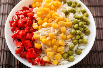 Plate with tasty boiled rice and vegetables on bamboo mat