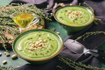 Bowls with tasty zucchini soup and peanuts on color background