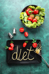 Plate with word DIET made of pasta with vegetables on color table