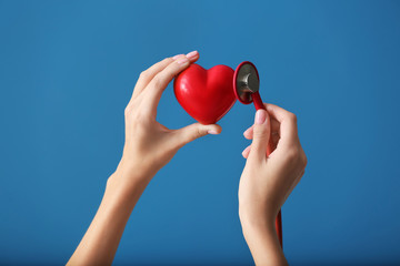 Hands of cardiologist with medical stethoscope and red heart on color background