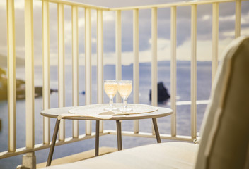 Set of two wine glasses with white wine on garden table outdoors on balcony with blue ocean and sky view, blurry background. Romantic luxurious vacation for two concept.