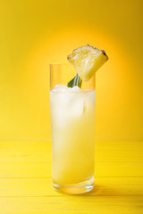 Glass of cold pineapple juice on yellow background