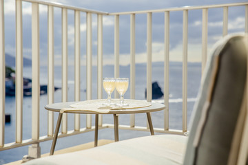 Set of two wine glasses with white wine on garden table outdoors on balcony with blue ocean and sky view. Romantic vacation for two concept.