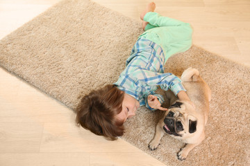 Little boy lying with cute pug dog on floor at home