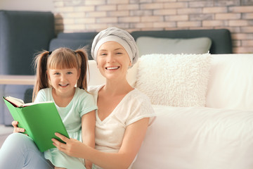 Little girl and her mother after chemotherapy reading book at home