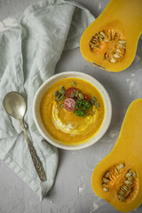 Pumpkin cream soup with parsley, tomatoes and seeds with spoon and towel at gray background
