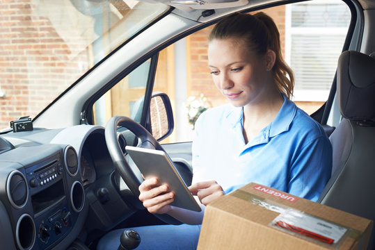 Female Courier In Van With Digital Tablet Delivering Package To House