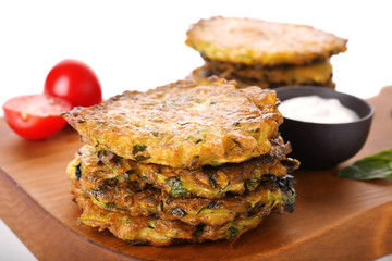 Board with tasty zucchini pancakes, sour cream and tomatoes on white background