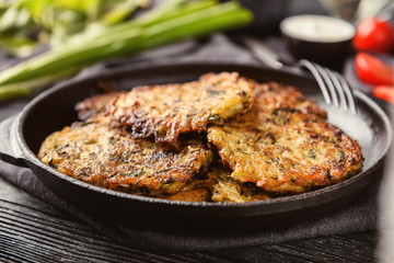 Frying pan with tasty zucchini pancakes on wooden table, closeup