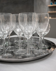 Wine glasses on silver metal tray on white table.