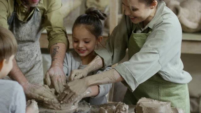 Tilt down of happy mother, father and children laughing and trying to make pottery in workshop