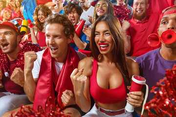 Young sport supporter happy fans cheering at stadium. Group of young woman and man support the football team during the match