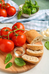 Board with delicious tomatoes, bread and fresh basil on white table