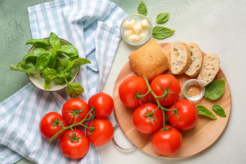 Board with delicious tomatoes, bread and fresh basil on light table