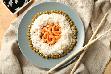 Plate with boiled rice, peas and tasty shrimps on table