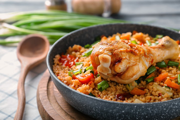 Frying pan with delicious boiled rice, chicken leg and vegetables on wooden board