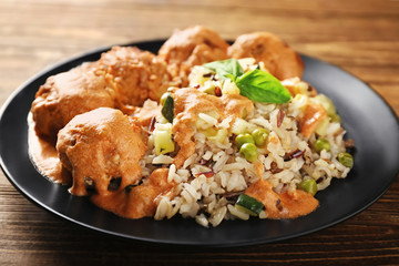 Plate with boiled rice, vegetables and meatballs on wooden table