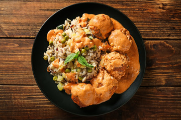 Plate with boiled rice, vegetables and meatballs on wooden table