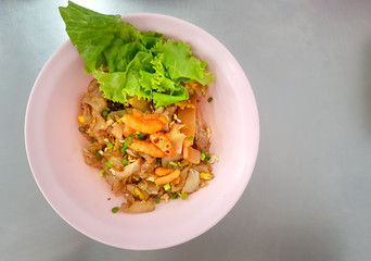 Chinese-Thai style dry noodle mixed with seafood and pork served in pink bowl.