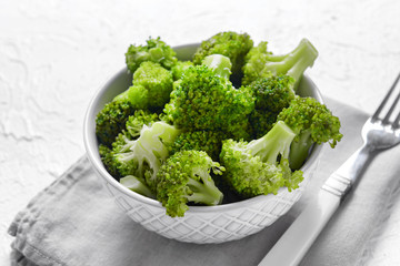 Bowl with fresh green broccoli on white table