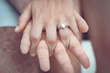 Engagement at the beach of tropical island. Close up of couple hands with silver ring on the finger.