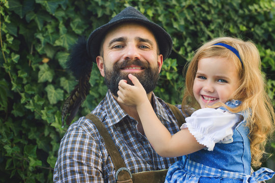 Beer Festival Oktoberfest.Man  in traditional bavarian clothes Lederhose with little girl on his hands in dirnndl. Papa and daughter
