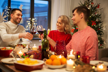 holidays and celebration concept - happy friends having christmas dinner at home, drinking red wine and clinking glasses