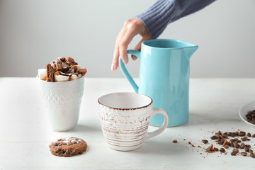 Woman with jug and cups of tasty cocoa on white table