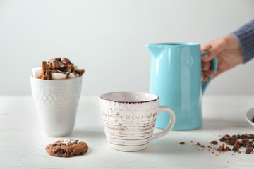 Woman with jug and cups of tasty cocoa on white table